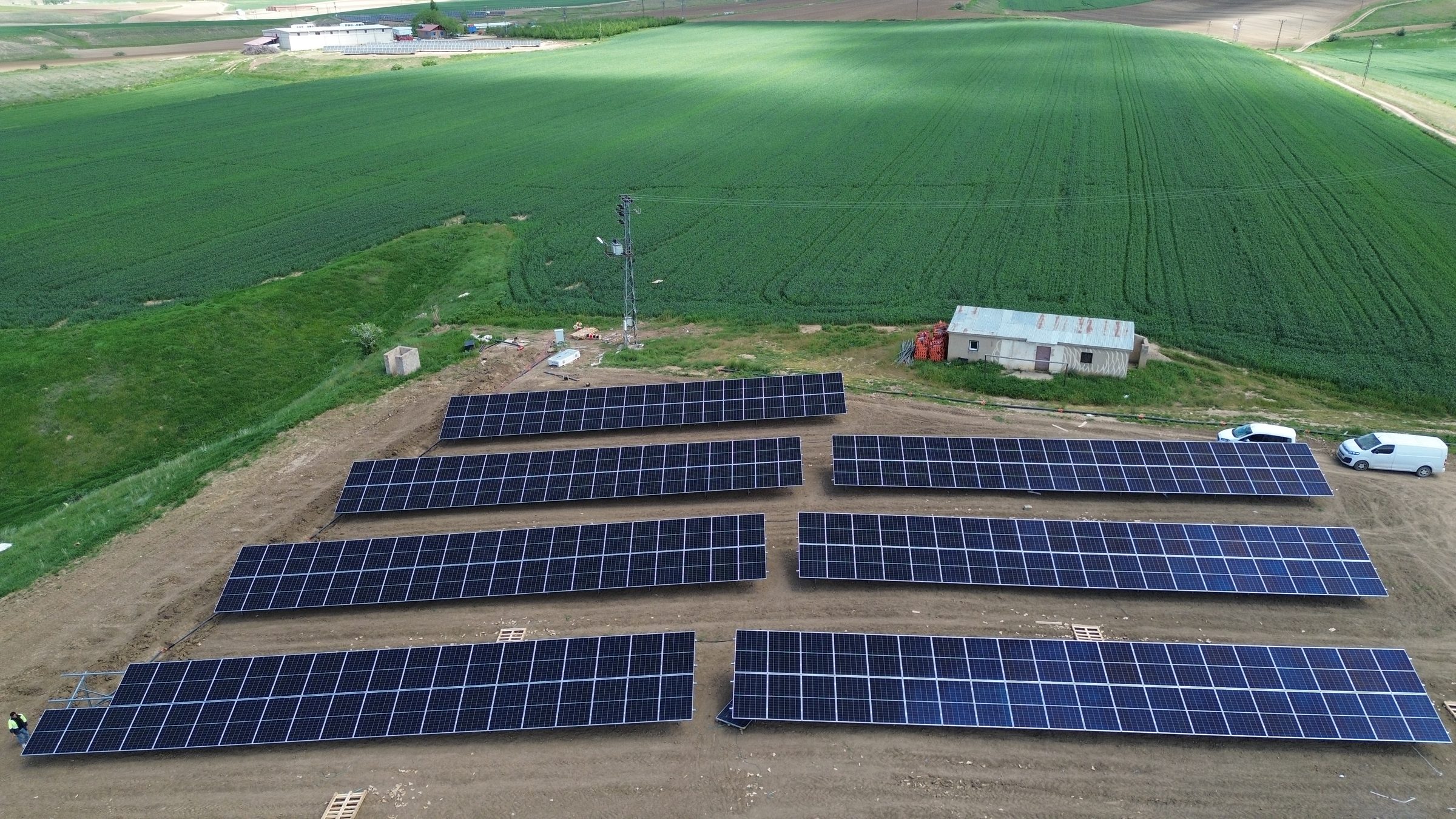 Buğday tarlası kenarında kurulu tarımsal güneş enerjisi santrali panel sıraları, drone görünümü